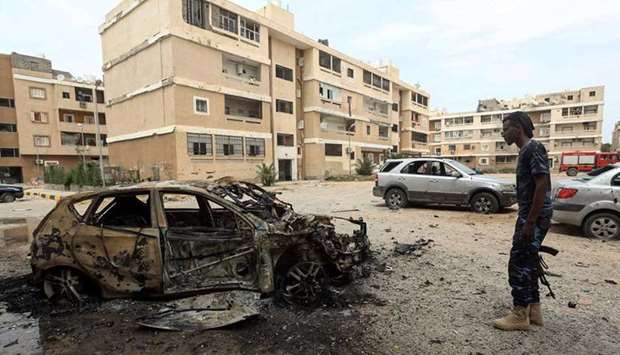 A fighter loyal to Libyau2019s UN-recognised Government of National Accord (GNA) stands next to a destroyed car following bombardment earlier in the day in the residential Bab Bin Ghashir neighbourhood of the capital Tripoli, yesterday. Right: Smoke fumes rise above buildings in the Libyan capital Tripoli, during  shelling.