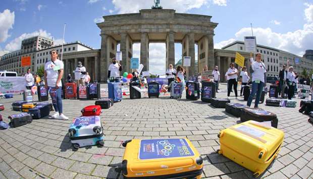 Travel agency workers stand next to suitcases decorated with protest posters in front of Berlinu2019s Brandenburg Gate.