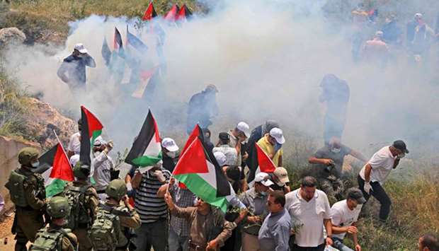 Palestinian protesters stand amid tear gas smoke fired by security forces during a demonstration against Israeli settlements, yesterday, in Al-Sawiya village, south of Nablus, in the occupied West Bank, as Palestinians mark the anniversary of Al-Nakba, or the u201ccatastropheu201d.