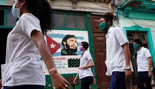 Medical students walk past an image of late Cuban president Fidel Castro as they check door to door for people with symptoms amid concerns about the spread of the coronavirus disease in downtown Havana, Cuba.