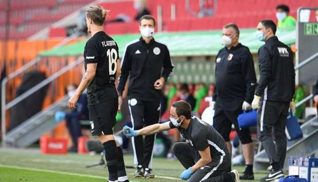 Augsburg's Croation defender Tin Jedvaj (L) receives medical attention during the German first division Bundesliga football match FC Augsburg v VfL Wolfsburg on May 16 in Augsburg, southern Germany, as the season resumed following a two-month absence due to the novel coronavirus pandemic