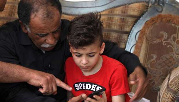 Hussein Dawabsha (left) sits with his grandson Ahmed, the survivor of the arson attack that killed his parents and 18-month-old brother, as they look at images on a phone at their home in the occupied West Bank village of Duma, yesterday, after a court convicted a Jewish settler on three counts of murder over the 2015 arson attack.
