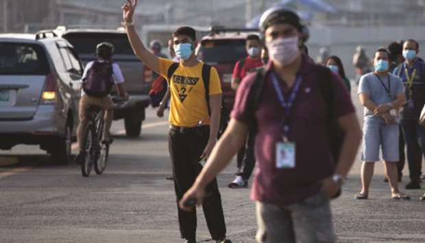 Workers wearing protective masks stand by to hitch a ride as some industries resumed operations with limited public transportation available, amid the Covid-19 outbreak, in Quezon City.