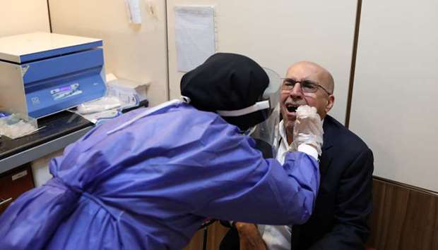 A member of the medical team wears a protective suit as she collects saliva of a man to be checked at a testing centre for coronavirus disease (Covid-19), in Tehran, yesterday.
