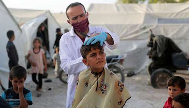 A volunteer hairdresser from the International Association for Relief and Development (ONSUR) wearing a face mask and gloves cuts the hair of an internally displaced boy, ahead of the Eid al-Fitr holiday, amid concerns over the spread of the coronavirus disease (Covid-19), at an IDP camp in Idlib, Syria.