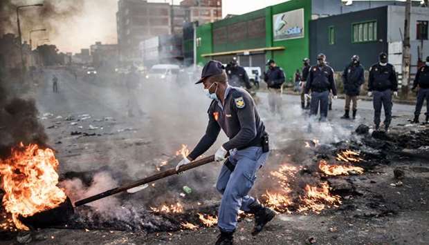 A South African police officer removes a burning barricade outside the Booysens informal settlement, during a protest in Johannesburg yesterday.
