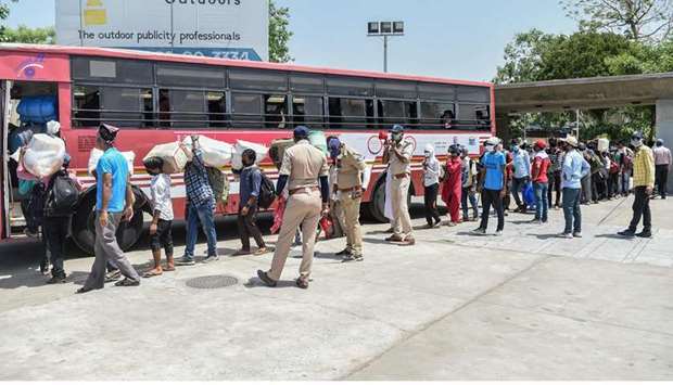 Police personnel stand guard as migrant workers and families board a bus going to the railway station in Ahmedabad yesterday.