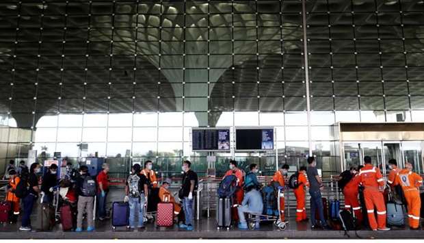 Passengers wearing protective face masks wait in a queue to enter Chhatrapati Shivaji International Airport, after the government allowed domestic flight services to resume, during an extended nationwide lockdown to slow the spread of the coronavirus disease, in Mumbai, India