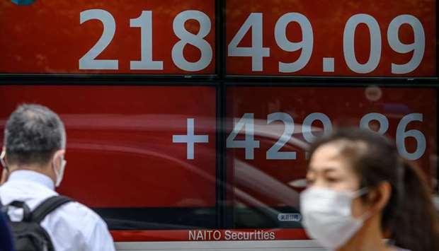 Pedestrians wearing face masks walk past an electric quotation board displaying the morning numbers of the Nikkei 225 Index on the Tokyo Stock Exchange. The TSE closed 2.3% higher at 21,916.31 points, a three-month high, yesterday.
