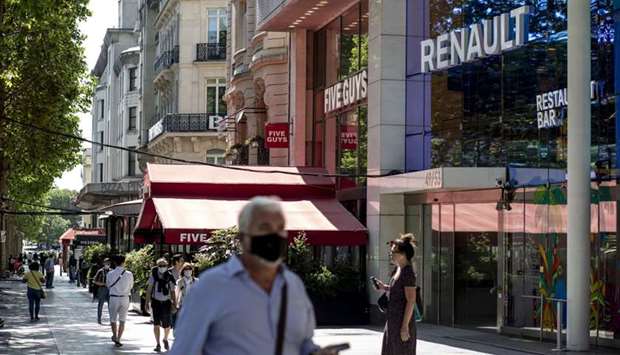 Pedestrians wear protective face masks outside the Renault flagship showroom on the Champs Elysee in Paris. Faced with a slump in demand that has been exacerbated by the coronavirus pandemic, the French carmaker detailed plans yesterday to find u20ac2bn ($2.22bn) in savings over the next three years.