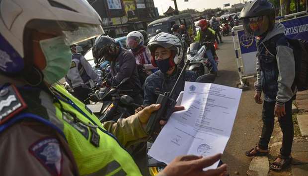 An Indonesian police officer inspects a document from a motorist heading toward the capital city of Jakarta, in Bekasi, West Java, yesterday, amid travel restrictions during the coronavirus pandemic.
