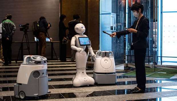 A reporter (R) records the greeting voice of a robot called ,Pepper, (C) with two other cleaning robots in the lobby of a hotel