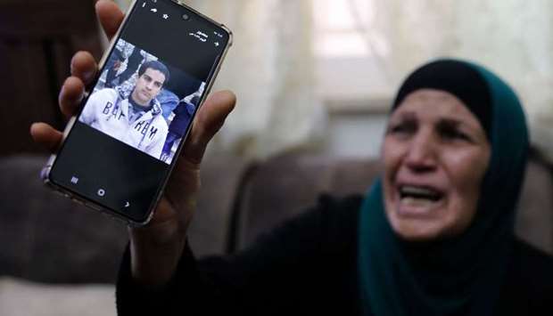The mother of a Palestinian man with special needs, reportedly shot dead, cries as she shows his picture on her mobile telephone.
