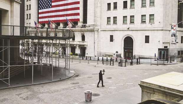 A pedestrian films himself while walking past the New York Stock Exchange on a nearly empty Wall Street.