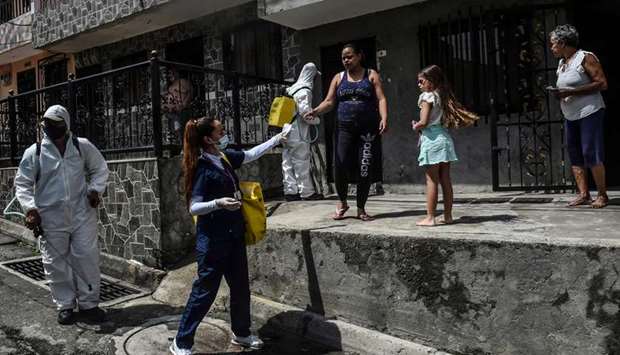 A health worker distributes face masks while workers wearing personal protective equipment disinfect the street as a preventive measure in the Santa Cruz neighbourhood of Medellin, Colombia.