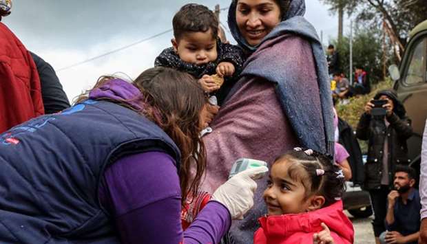 A woman checks the temperature of a child as other migrants wait to be transferred from the island of Lesbos to the Greek mainland yesterday.