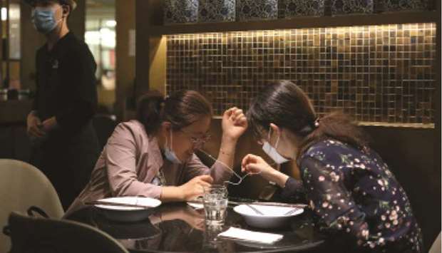 Women wearing face masks look at a cellphone while waiting to be served during lunchtime at a restaurant, in Beijing.