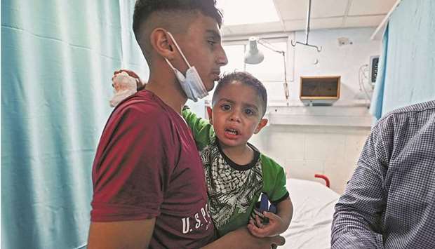 A Palestinian youth comforts an injured boy receiving medical care at Al Shifa hospital after an Israeli air strike in Gaza city, yesterday. Right: A Palestinian man gestures as he inspects a damaged building following an air strike, amid a flare-up of violence, in Gaza City.