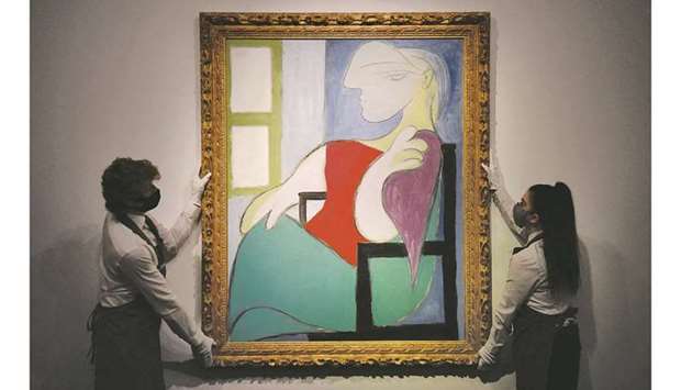 This photo taken on April 22 shows gallery workers with the Femme assise pru00e8s du2019une fenu00eatre (Marie-Thu00e9ru00e8se) by Pablo Picasso during a photocall at Christieu2019s auction house in central London.