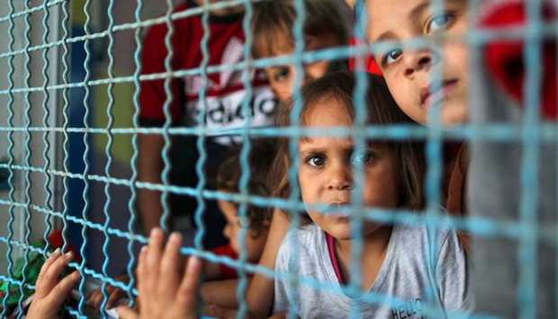 Palestinian children, who fled their homes due to Israeli air and artillery strikes, look through a window fence at a United Nations-run school where they take refuge, in Gaza City.