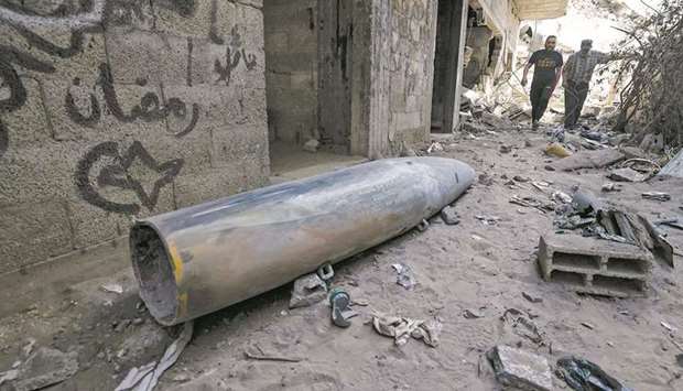 Palestinian men walk amid the rubble behind an unexploded bomb (foreground) dropped by an Israeli F-16 warplane on Gaza Cityu2019s Rimal neighbourhood.
