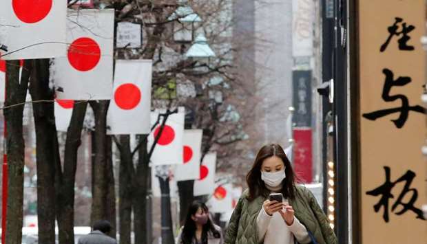 Pedestrians wearing protective masks, following the coronavirus disease (Covid-19) outbreak, walk underneath Japanese national flags at a shopping district in Tokyo