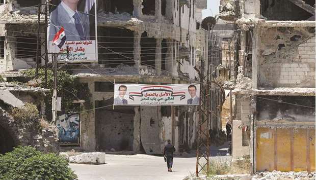 A man walks past banners depicting Syriau2019s President Bashar al-Assad, near damaged buildings, ahead of todayu2019s presidential election, in Homs.