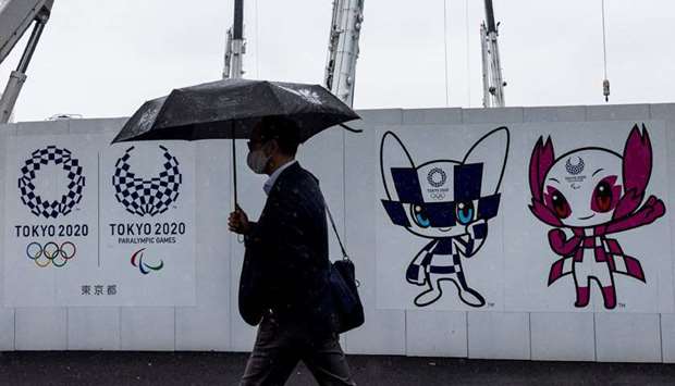 A pedestrian walks past a Tokyo 2020 Olympic and Paralympic Games decoration board bearing illustrations of Games logo and mascots in Tokyo