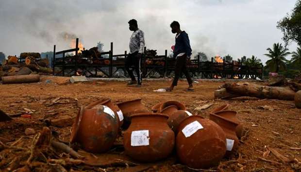 Men walk past burning pyres of persons who died due to the coronavirus disease, at a crematorium ground in Tavarekere on the outskirts of Bengaluru, India
