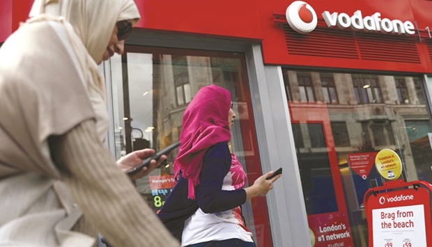 People hold their phones as they pass a Vodafone  store in London. Vodafone said it looked forward to building a long-term relationship with UAE-based e&.