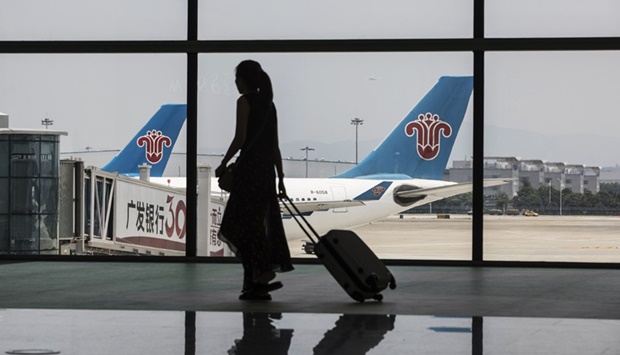 A woman carrying luggage is silhouetted as she walks past aircraft operated by China Southern Airlines sitting on the tarmac at Terminal 2 of the Guangzhou Baiyun International Airport in China.