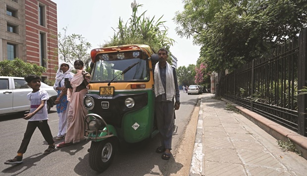 Pedestrians walk past as autorickshaw driver Mahender Kumar stands beside his vehicle with a u2018gardenu2019 on its roof, in New Delhi yesterday.