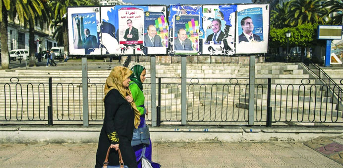 Women walk past election posters in Algiers yesterday. 