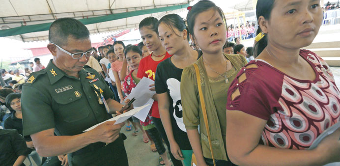 Thai military officer (left) checks the document of Myanmar migrant workers queuing at the one stop service for the registration of migrant workers in