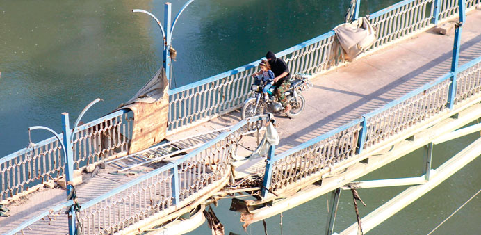 A rebel fighter and a child cross a damaged bridge in Syriau2019s eastern town of Deir al-Zor yesterday.