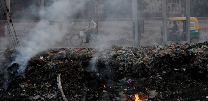 People pass by garbage that is dumped and burnt on the roadside in Faridabad