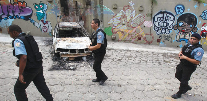 Brazilian policemen walk by a burnt vehicle in the Copacabana sector which appears calm after Tuesday nightu2019s violent riots.