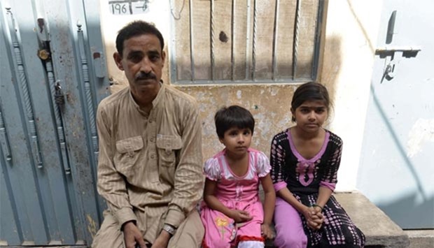 Pakistani schoolgirl Maham (right), who was taught by a teenager who was set on fire by her mother, poses for a photograph alongside classmate Amina (centre) and her father Muhammad Asghar outside the house where their teacher lived in Lahore.
