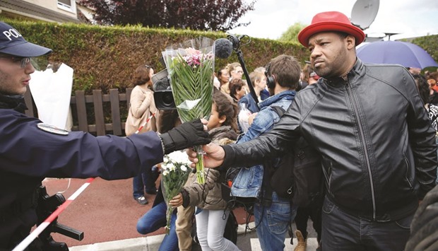 A police officer is handed a bouquet outside the house in Magnanville where a man claiming allegiance to the Islamic State group killed a French policeman and his partner on the night of June 13.