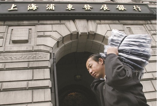 A Chinese man hauling goods passes by the front door of Pudong Development Bank in Shanghai. Pudong Development Bank was the first to issue 20bn yuan in Chinau2019s interbank bond market in January and will choose projects focused on curbing pollution and recycling.