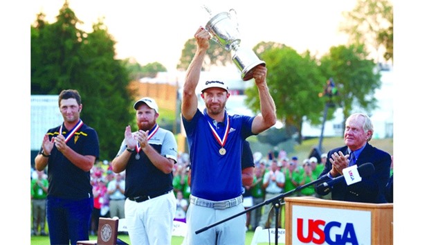 Dustin Johnson of the United States poses with the winneru2019s trophy after winning the US Open as Shane Lowry (C) of Ireland and Amateur Jon Rahm (L) of Spain look on.