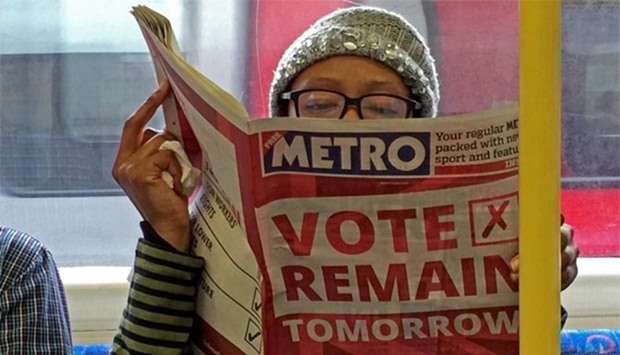 A woman reads a newspaper on the underground in London on Wednesday with a 'vote remain' advert for the Brexit referendum.