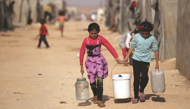 Internally displaced Syrian girls carry water containers in Jrzinaz camp, in the southern part of Idlib, Syria.