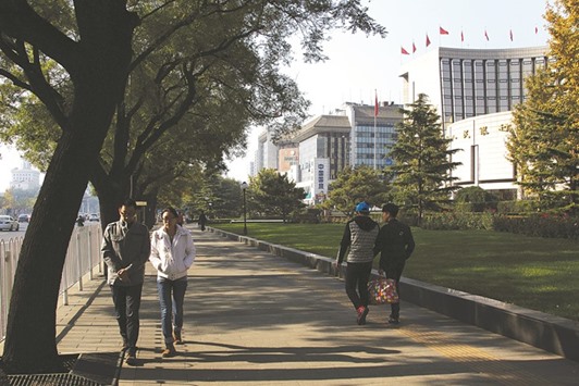 Pedestrians walk past the Peopleu2019s Bank of China headquarters (right) in Beijing. The PBoC has promoted NPL-backed securities as one way to free up lendersu2019 balance sheets and shift bad debt to institutions better able to cope with the risks.