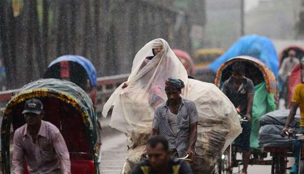 Bangladeshi rickshaw pullers make their way with commuters during a monsoon rain in Dhaka