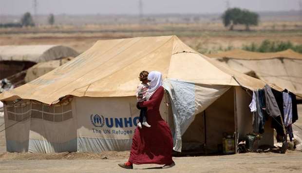 A Syrian woman displaced from Raqa walks carrying a child at the al-Karamah aid camp