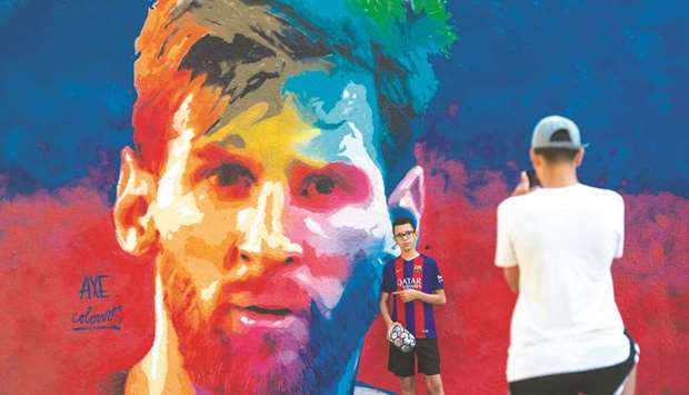 A boy poses for a photo beside a graffiti of Barcelonau2019s Argentinian forward Lionel Messi in Barcelona. (AFP)