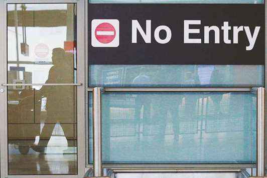 International travellers are reflected in a closed door as they arrive on the day that the US travel ban, approved by the Supreme Court, goes into effect, at Logan Airport in Boston, Massachusetts.