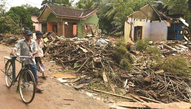 Residents walk past damaged homes following flooding in Yatagampitiya village in Bulathsinhala yesterday.