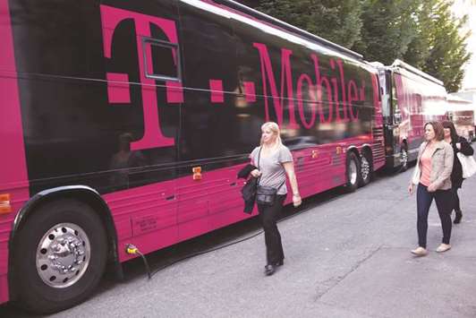 Women walk past buses displaying T-Mobile logos outside the Paramount Theatre in Seattle. T-Mobile CFO Braxton Carter said that a merger with Sprint could yield more than $30bn in cost savings while u201cturbo-chargingu201d T-Mobileu2019s ability to challenge larger rivals.